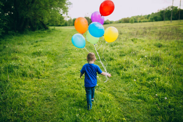 Fotografi av barn som går på en åker med ballonger i hånda