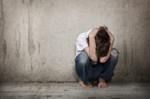 Ungdom som sitter på huk inntil en vegg med hodet i hendene