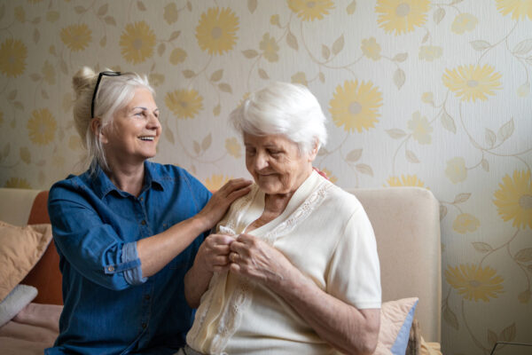 Fotografi av kvinne som hjelper eldre kvinne med påkledning i et rom
