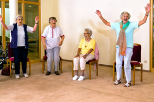 En gruppe eldre damer holder på med enkel fysisk aktivitet i form av stol-trim.