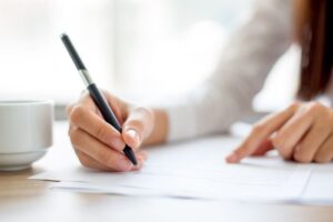 Person med pen i hånden som skriver på papir Foto: Shutterstock