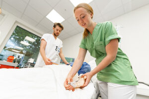To sykepleiestudenter foretar vitale målinger på en dukke i forbindelse med ferdighetstrening.