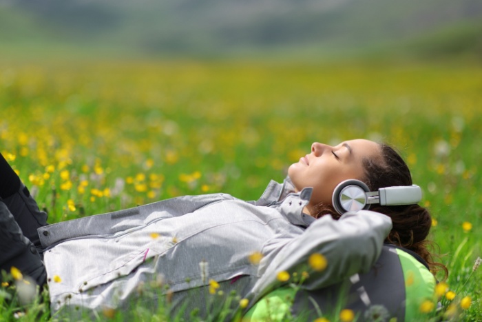 Ung dame ligger i blomstereng og lytter til noe med øretelefoner