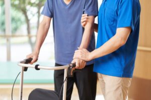 Eldre person går med rullator med støtte fra fysioterapeut Foto: Shutterstock