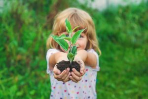 Bilde av ung jente som holder en haug jord i hånda hvor en plante vokser opp.