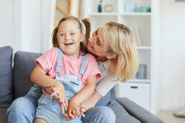 Fotografi av mor og barn. Barnet har downs-syndrom og sitter på fanget til mor. Begge smiler